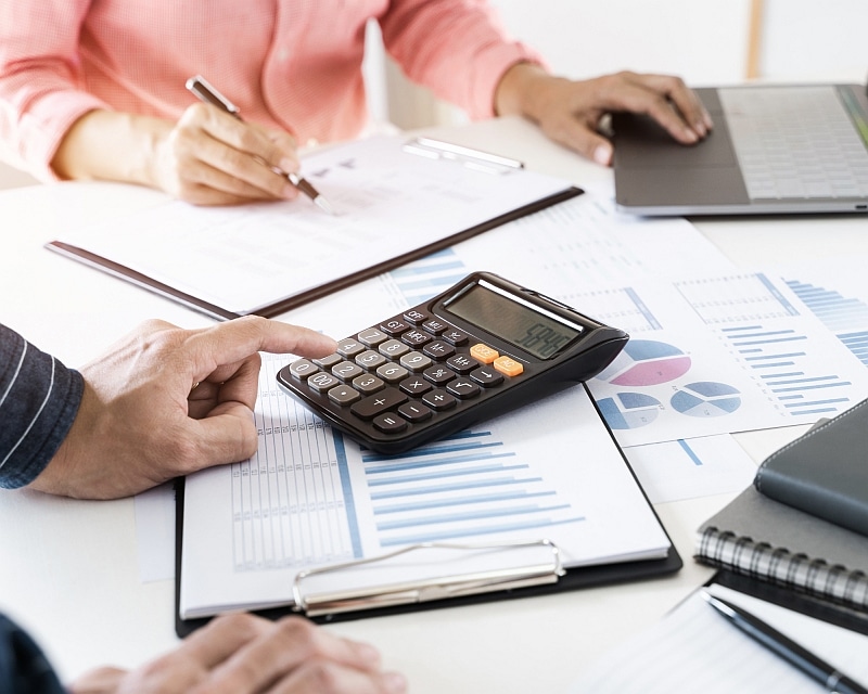 Two people are sitting at a table with documents, a laptop and a calculator